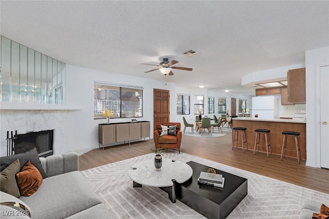 living room featuring ceiling fan, a premium fireplace, a textured ceiling, and light hardwood / wood-style floors