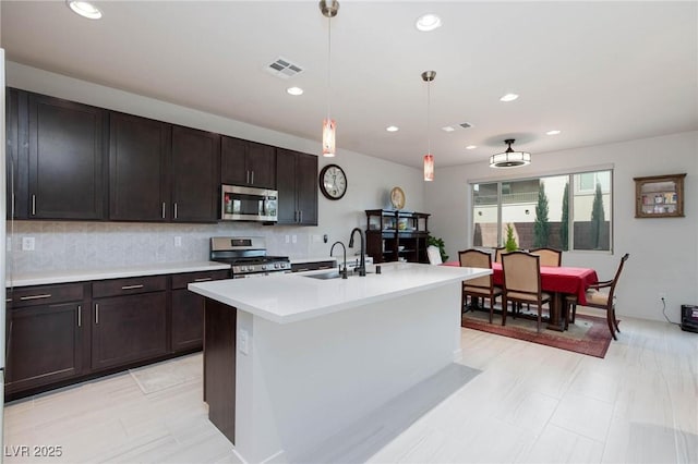 kitchen featuring decorative backsplash, appliances with stainless steel finishes, sink, decorative light fixtures, and a center island with sink