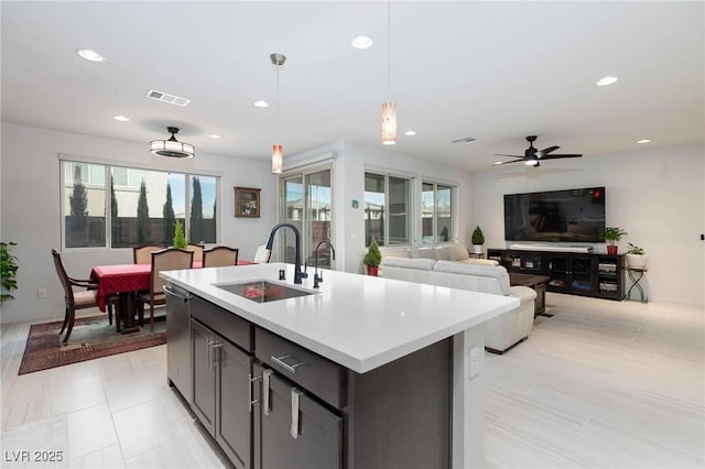 kitchen featuring sink, hanging light fixtures, stainless steel dishwasher, ceiling fan, and an island with sink