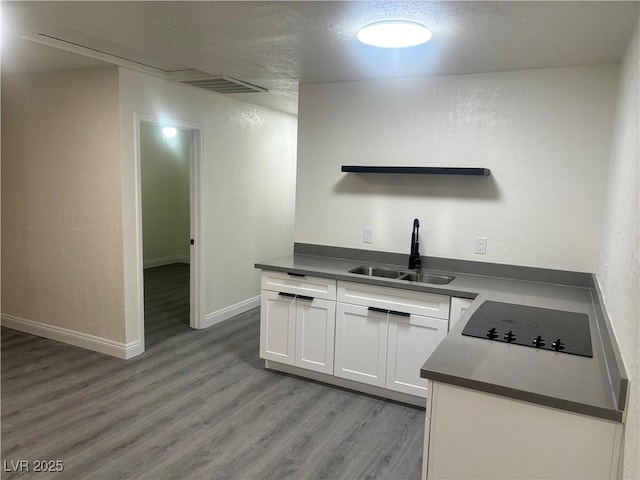 kitchen with white cabinets, black electric cooktop, sink, and light hardwood / wood-style flooring