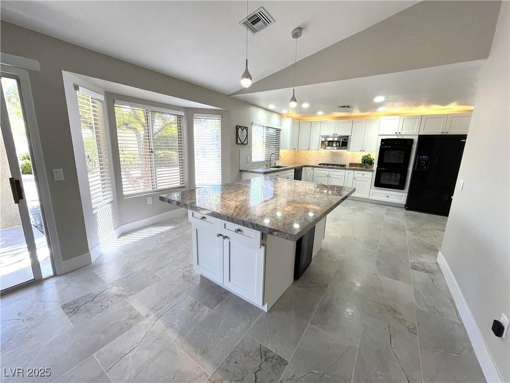 kitchen featuring dark stone countertops, pendant lighting, vaulted ceiling, white cabinets, and black appliances