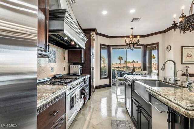 kitchen with pendant lighting, high end appliances, backsplash, light stone countertops, and a notable chandelier