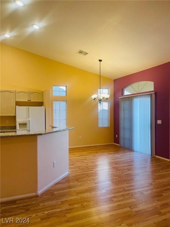 kitchen featuring pendant lighting, a notable chandelier, light hardwood / wood-style floors, white fridge with ice dispenser, and vaulted ceiling