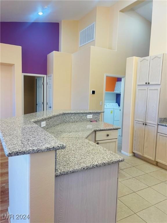 kitchen with light tile patterned flooring, light stone counters, a center island, high vaulted ceiling, and independent washer and dryer