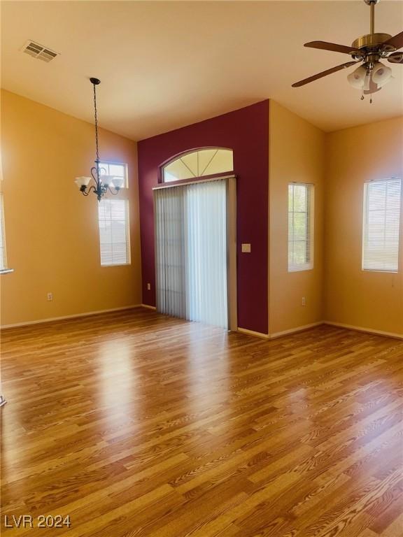 empty room with vaulted ceiling, ceiling fan with notable chandelier, and hardwood / wood-style floors