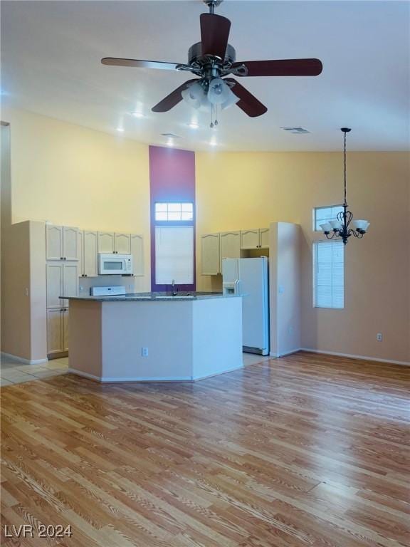 kitchen with hanging light fixtures, white appliances, light wood-type flooring, and a high ceiling