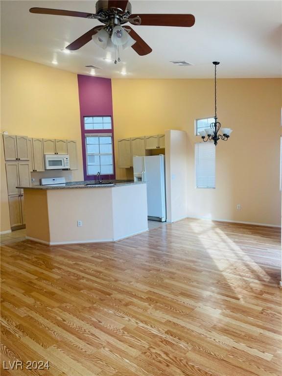 unfurnished living room featuring a high ceiling, sink, ceiling fan with notable chandelier, and light wood-type flooring