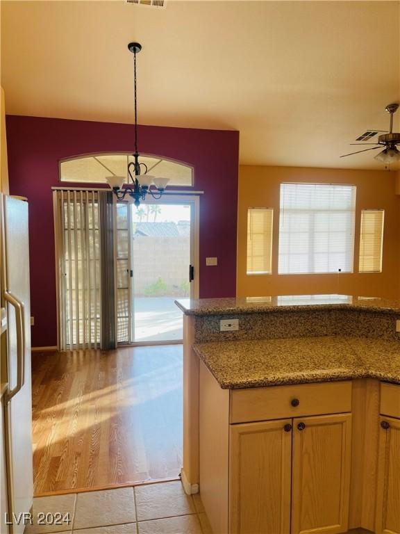 kitchen with light tile patterned flooring, stone countertops, decorative light fixtures, white refrigerator, and ceiling fan with notable chandelier