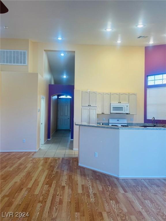 kitchen with white cabinetry, a high ceiling, stove, light stone countertops, and light hardwood / wood-style flooring