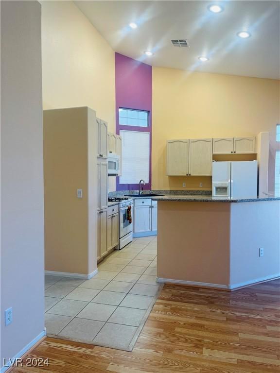 kitchen with sink, light wood-type flooring, a towering ceiling, white appliances, and dark stone counters