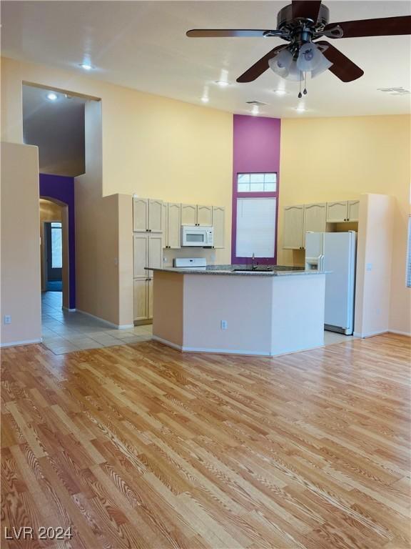 unfurnished living room with sink, light hardwood / wood-style flooring, ceiling fan, and a high ceiling