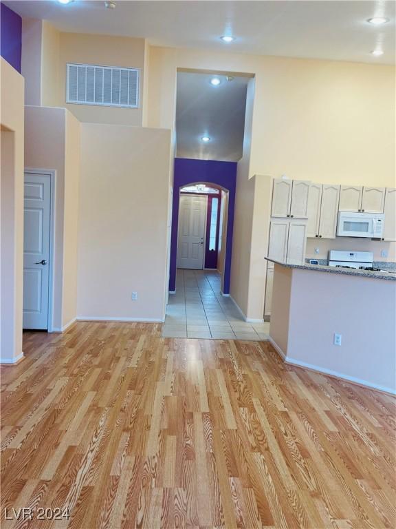 interior space with white cabinetry, stove, a towering ceiling, and light hardwood / wood-style floors