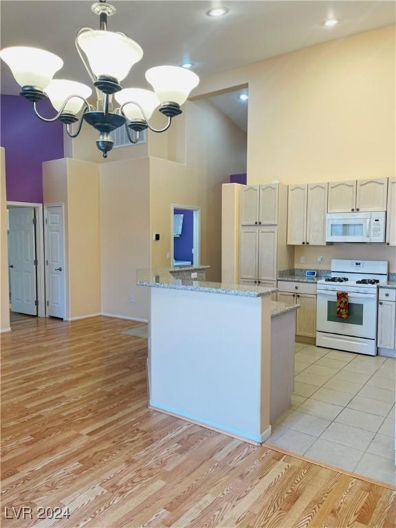 kitchen with decorative light fixtures, high vaulted ceiling, light wood-type flooring, a notable chandelier, and white appliances