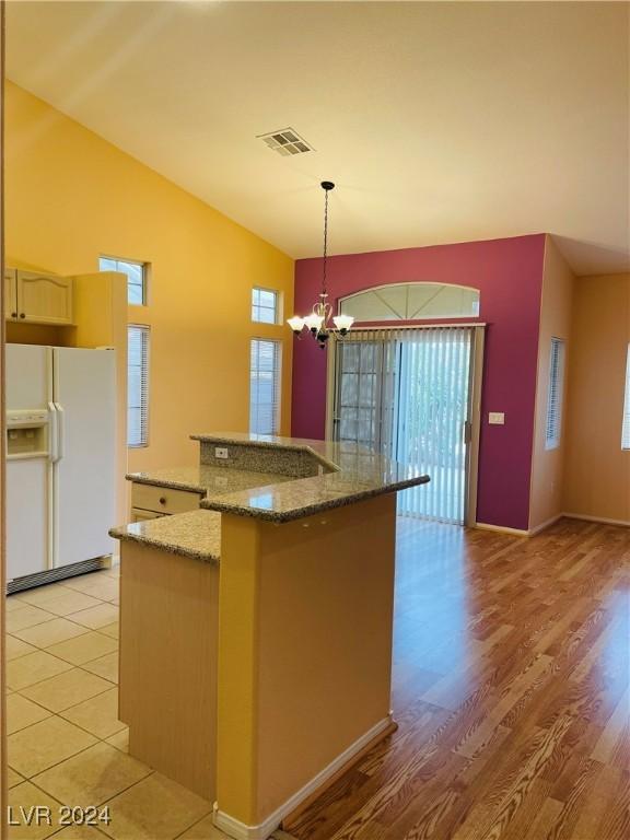 kitchen with an island with sink, hanging light fixtures, white refrigerator with ice dispenser, a notable chandelier, and plenty of natural light