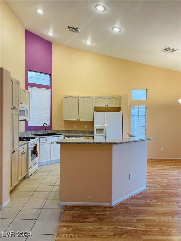 kitchen featuring a kitchen island, high vaulted ceiling, sink, light stone counters, and white appliances