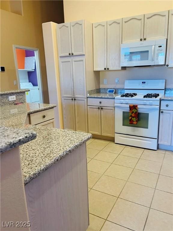 kitchen with light stone countertops, washer and dryer, light tile patterned floors, and white appliances