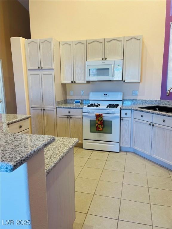 kitchen with sink, light stone counters, white appliances, and light tile patterned floors