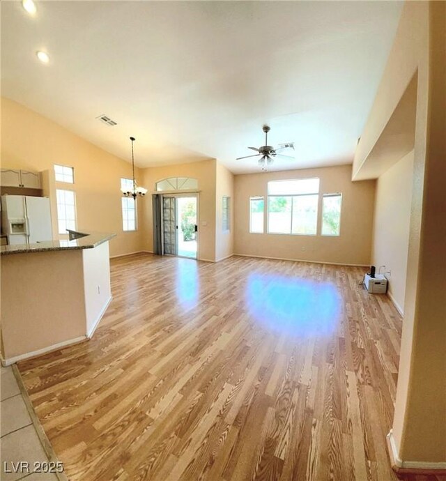 unfurnished living room with light wood-type flooring, a ceiling fan, baseboards, a chandelier, and lofted ceiling