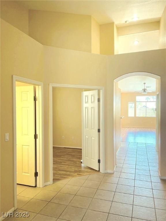 corridor featuring light tile patterned floors, arched walkways, baseboards, and a towering ceiling