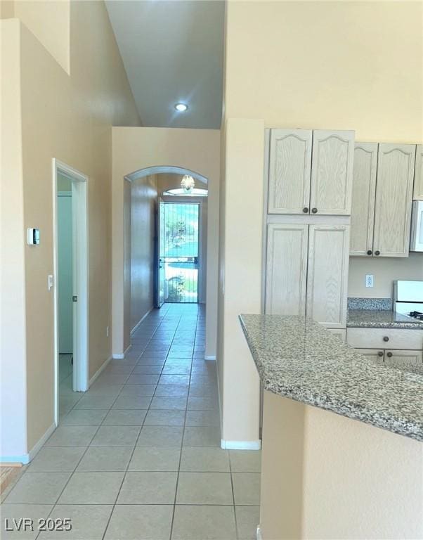 kitchen with light tile patterned flooring, white microwave, arched walkways, light stone countertops, and baseboards