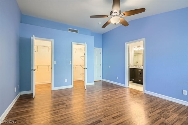 unfurnished bedroom featuring a walk in closet, ceiling fan, connected bathroom, dark hardwood / wood-style flooring, and a closet