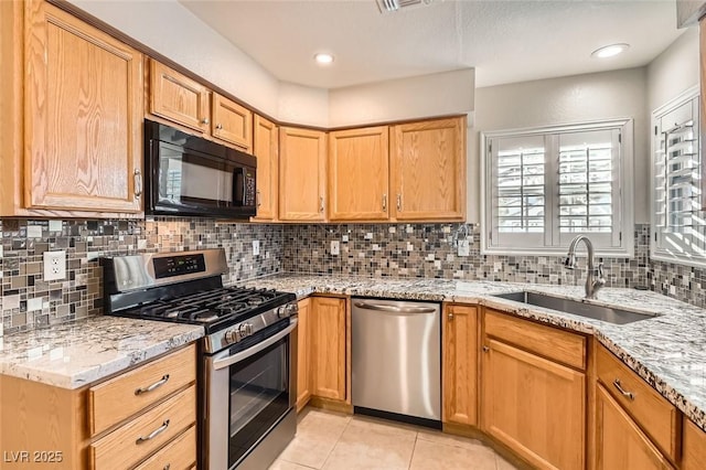 kitchen with sink, decorative backsplash, light tile patterned floors, light stone countertops, and appliances with stainless steel finishes