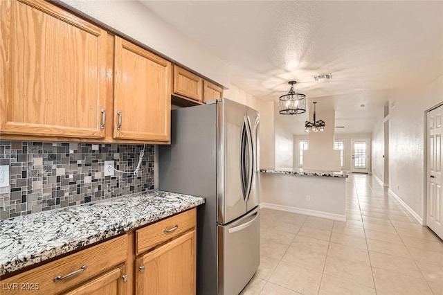 kitchen with stainless steel refrigerator, an inviting chandelier, light stone counters, decorative backsplash, and light tile patterned floors