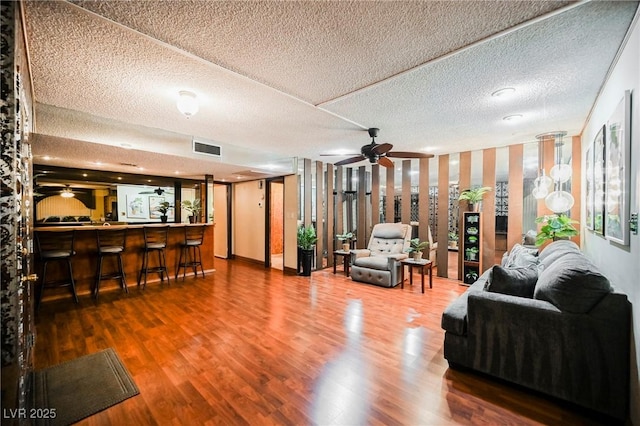 living room with hardwood / wood-style flooring, ceiling fan, a textured ceiling, and indoor bar