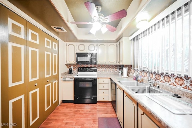 kitchen with black appliances, sink, ceiling fan, a tray ceiling, and light hardwood / wood-style floors