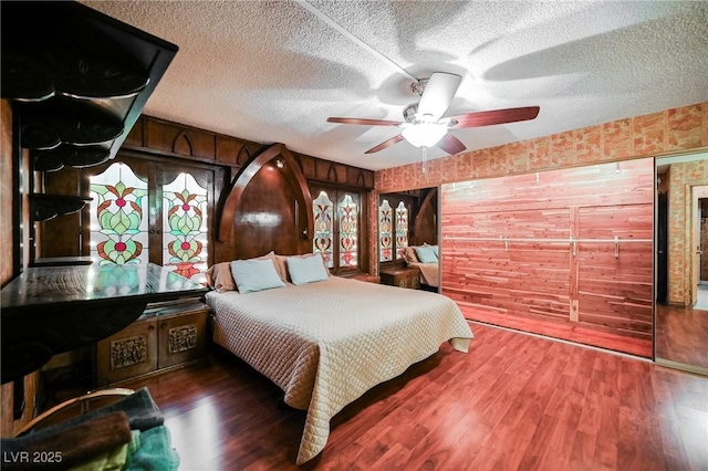 bedroom with wooden walls, hardwood / wood-style floors, ceiling fan, and a textured ceiling