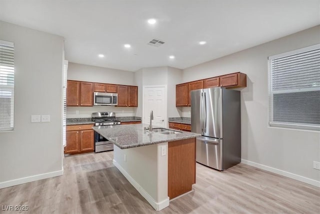 kitchen with sink, stainless steel appliances, light stone counters, light hardwood / wood-style flooring, and a center island with sink