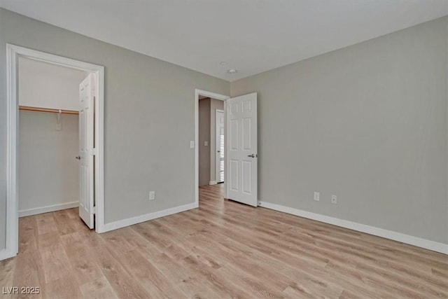 unfurnished bedroom featuring a walk in closet, a closet, and light hardwood / wood-style floors