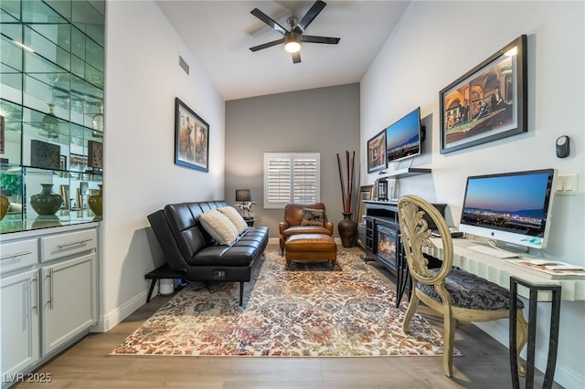 office area with a fireplace, light wood-type flooring, and ceiling fan