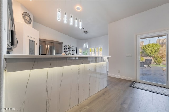 kitchen featuring plenty of natural light, stainless steel fridge, light hardwood / wood-style flooring, and decorative light fixtures