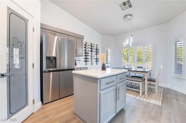 kitchen with pendant lighting, gray cabinetry, stainless steel refrigerator with ice dispenser, light wood-type flooring, and a kitchen island