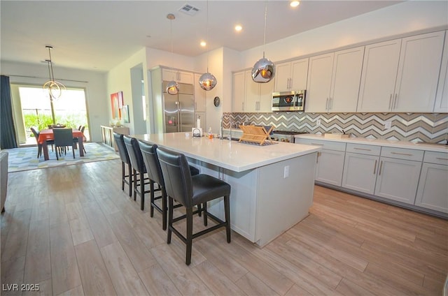 kitchen with tasteful backsplash, pendant lighting, stainless steel appliances, and a kitchen island with sink