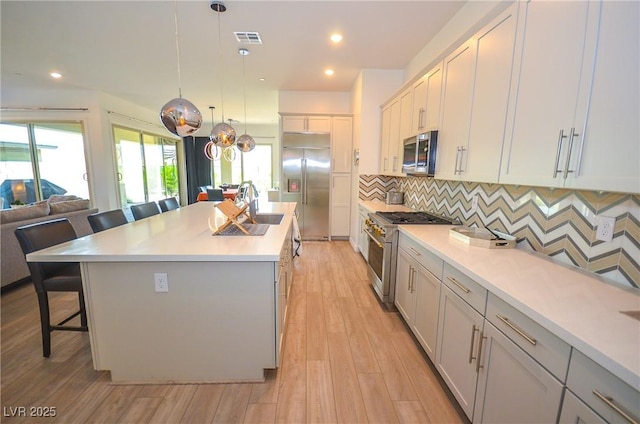 kitchen with a center island, backsplash, decorative light fixtures, premium appliances, and a kitchen bar