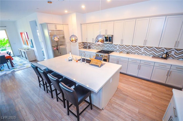 kitchen with pendant lighting, stainless steel appliances, a center island with sink, and a breakfast bar area