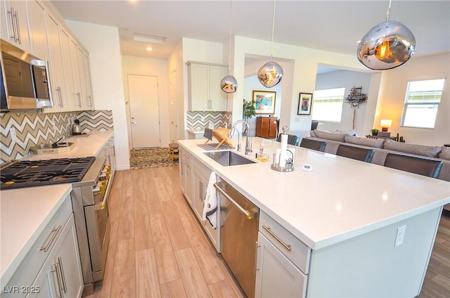 kitchen featuring sink, hanging light fixtures, stainless steel appliances, backsplash, and an island with sink