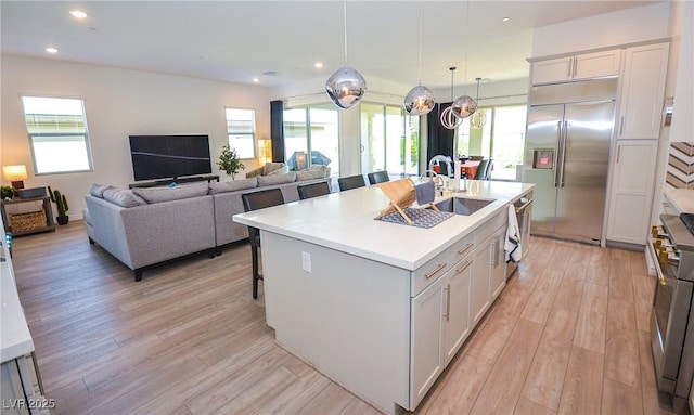 kitchen with a center island with sink, high end appliances, white cabinetry, and sink