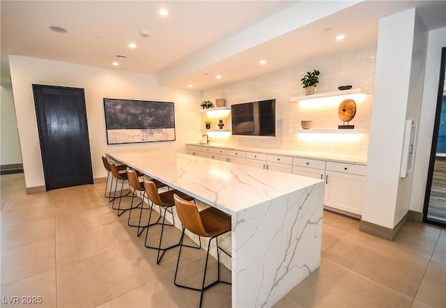 kitchen featuring light stone countertops, backsplash, kitchen peninsula, a breakfast bar area, and white cabinets