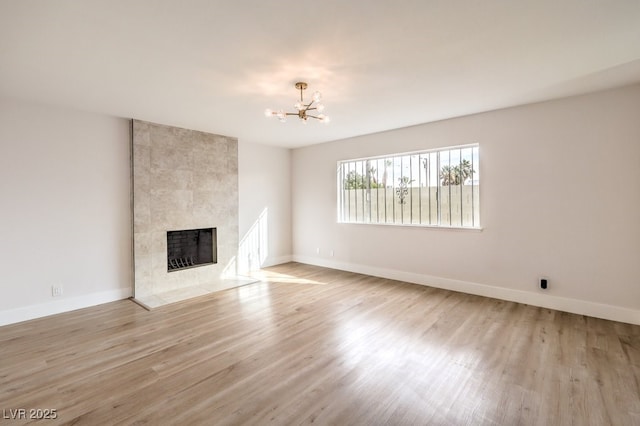 unfurnished living room with a tiled fireplace, light hardwood / wood-style flooring, and a chandelier