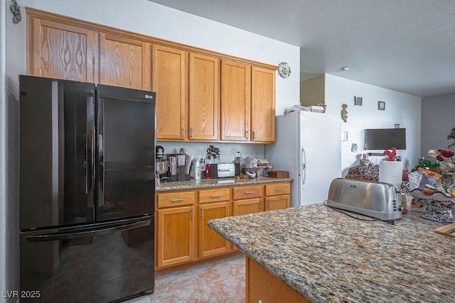 kitchen with black refrigerator, dark stone countertops, white refrigerator, and light tile patterned flooring