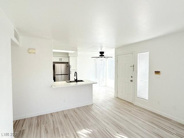 unfurnished living room featuring ceiling fan, light hardwood / wood-style floors, and sink