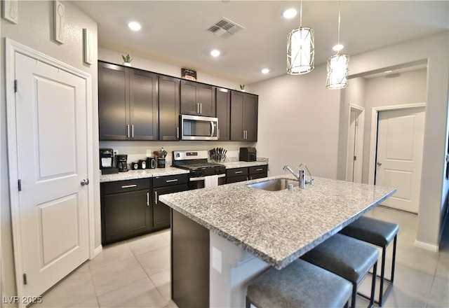 kitchen with sink, an island with sink, decorative light fixtures, a kitchen bar, and appliances with stainless steel finishes