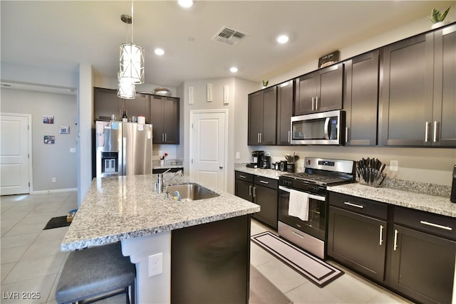 kitchen with appliances with stainless steel finishes, dark brown cabinets, a kitchen island with sink, sink, and light tile patterned floors