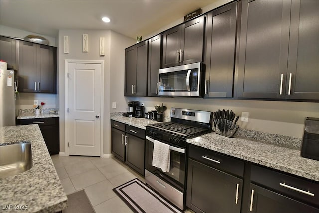 kitchen with sink, light tile patterned floors, appliances with stainless steel finishes, light stone counters, and dark brown cabinetry