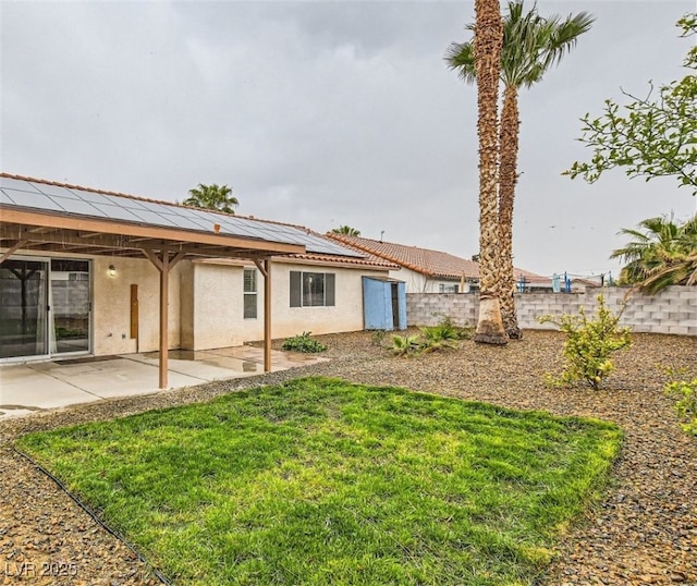 back of property with solar panels, a yard, and a patio area