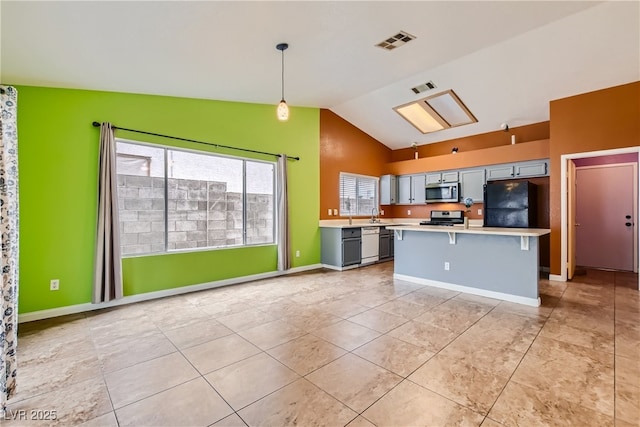 kitchen with gray cabinetry, stainless steel appliances, vaulted ceiling, decorative light fixtures, and a center island