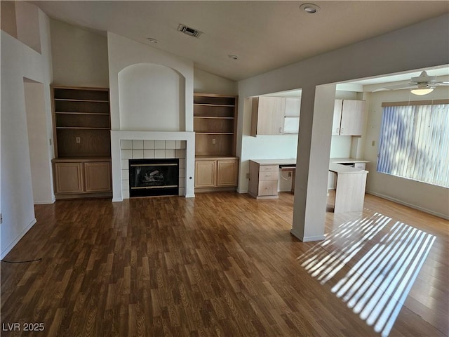 unfurnished living room featuring lofted ceiling, ceiling fan, dark wood-type flooring, and a tiled fireplace